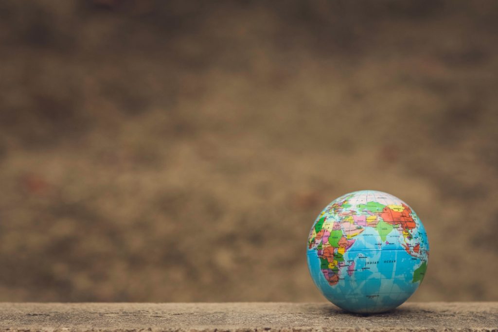 A small, colorful desk globe sitting on a textured concrete surface with a softly blurred background.